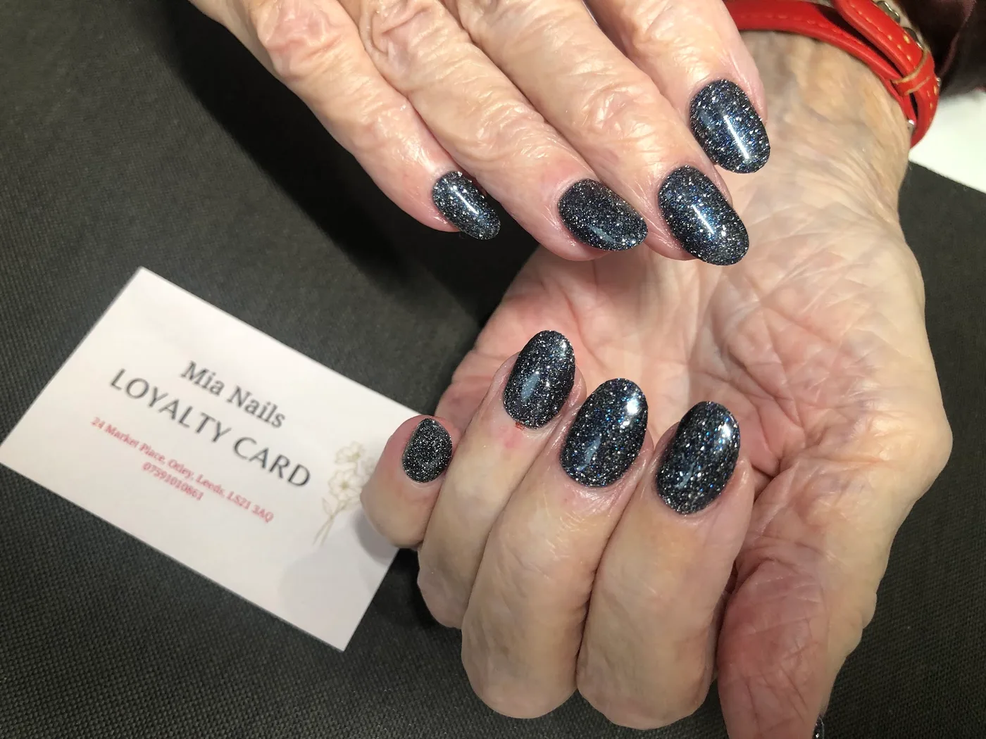 Dark glitter nails beside a Mia Nails loyalty card